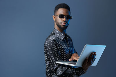 Young man using laptop while standing against blue background