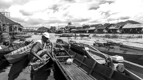 Man with boats moored at harbor against sky in city