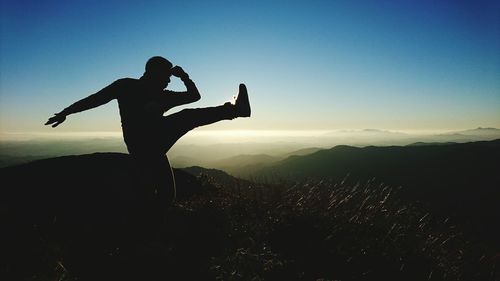 Silhouette of man kicking against sky