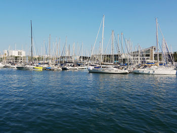 Sailboats moored on harbor against clear blue sky