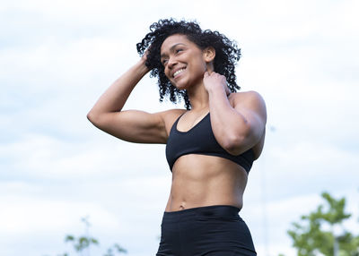 Delighted african american muscular female stretching arms and warming up before training in park while looking away