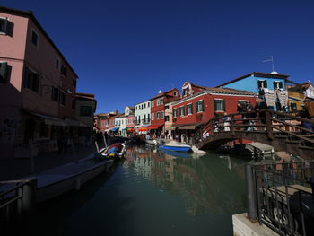 Canal amidst buildings against blue sky