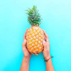 Cropped image of hand holding apple against blue background