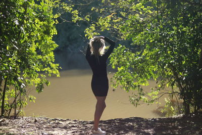 Rear view of woman standing at lakeshore amidst trees
