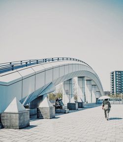 Rear view of people walking on bridge in city against clear sky