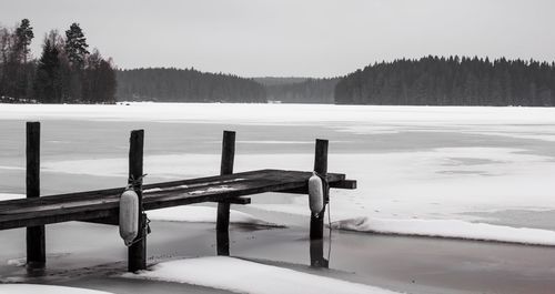 Wooden posts in lake against sky during winter