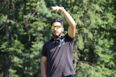 Portrait of young man wearing sunglasses standing against plants