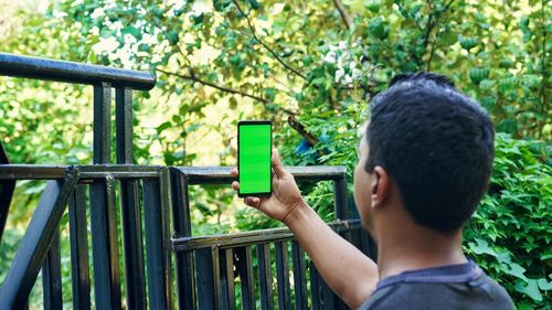 Young indian man taking selfie and showing a green screen cell phone with rural village life 