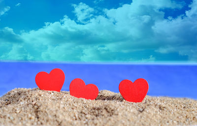 Close-up of heart shape on sand at beach against blue sky