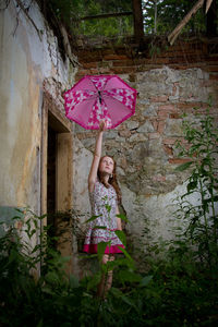 Portrait of girl holding pink while standing against wall