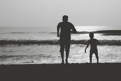 Rear view of father with son running at sea shore against sky