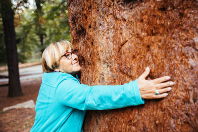 Side view of a woman against tree trunk