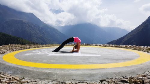 Woman exercising on helipad against mountain