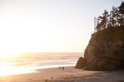 People walking at beach against clear sky during sunset