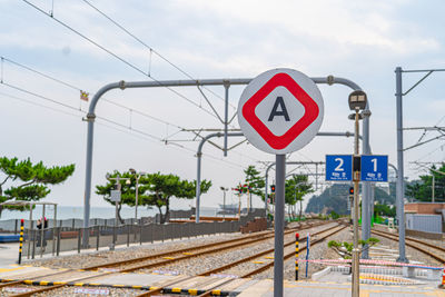 Road sign by railroad tracks against sky