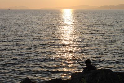 Rear view of man fishing at calm lake
