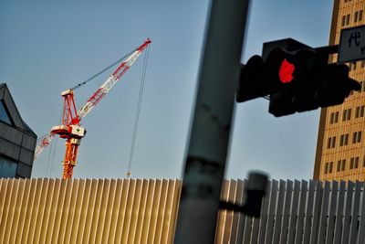 Low angle view of crane by building against clear sky