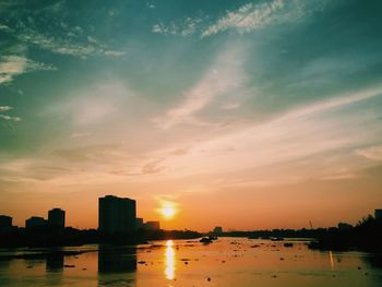 Silhouette buildings by river against sky during sunset