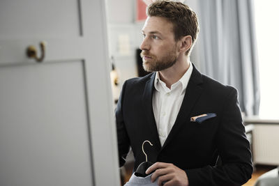 Mature businessman holding coathanger standing in hotel room