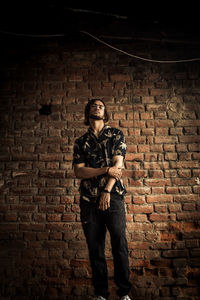 Full length portrait of young man standing against brick wall