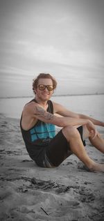 Portrait of young man sitting at beach against sky