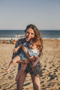 Portrait of young woman and baby standing at beach