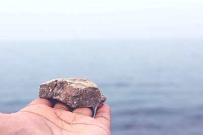 Close-up of hand holding stone against sea