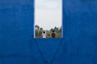 Rear view of friends against sky seen through window