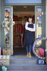 Smiling female owner looking away while standing at entrance of store