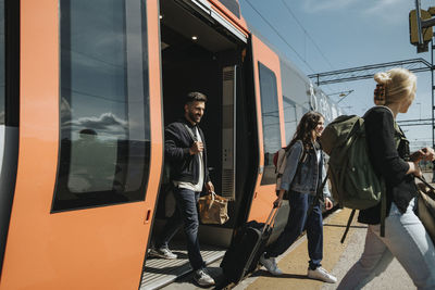 Smiling man with family disembarking from train at station