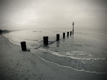 Wooden posts on beach against sky