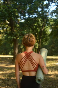 Rear view of woman standing with exercise mat against trees