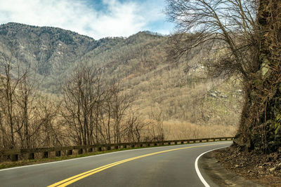 Empty road amidst trees against sky