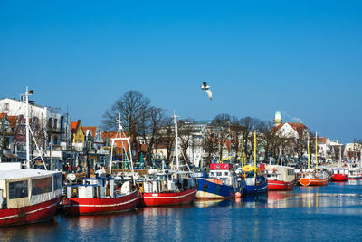 Boats moored at harbor against clear blue sky