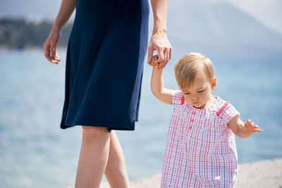 Cute daughter with mother walking at beach