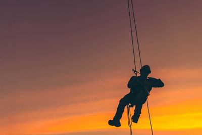 Silhouette man with rope against orange sky