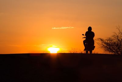 Silhouette person riding motor scooter against sky during sunset