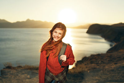 Portrait of smiling young woman standing against sky during sunset