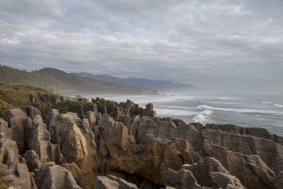 Scenic view of pancake rocks at beach against cloudy sky