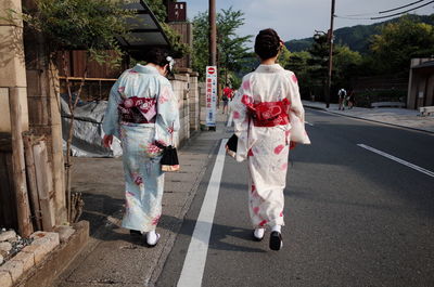 Rear view of geisha walking on road against cloudy sky