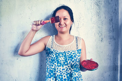 Portrait of a smiling young woman standing against wall