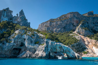 Rock formations in sea against clear blue sky