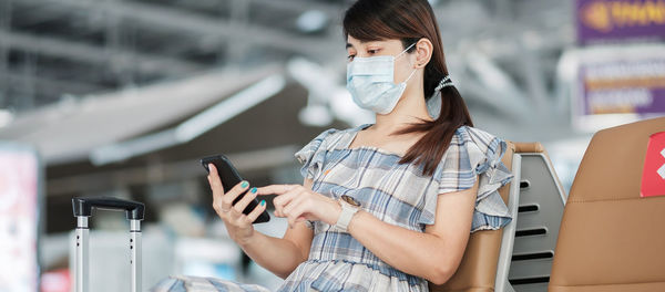 Woman wearing flu mask using smart phone sitting at airport