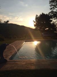 Swimming pool by lake against sky during sunset