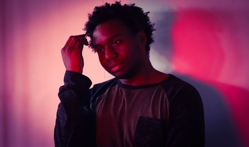 Thoughtful young man standing against red wall