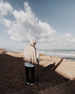 Rear view of senior man standing at beach against sky