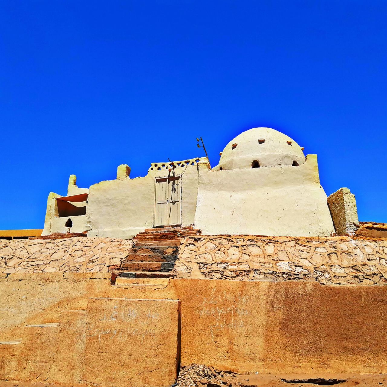 architecture, built structure, history, sky, fortification, clear sky, building exterior, the past, blue, travel destinations, building, ancient history, travel, nature, ancient, sunny, temple, religion, no people, fort, historic site, tourism, wall, belief, monument, place of worship, outdoors, sunlight, day, ruins, rock, sand, old ruin, spirituality, archaeological site, old, stone material, landmark, temple - building, low angle view, surrounding wall, fortified wall