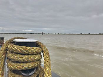 Rope tied to wooden post in sea against sky