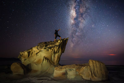 Rear view of man standing on cliff by sea against star field