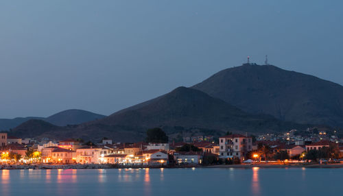 Illuminated buildings by sea against clear sky at night